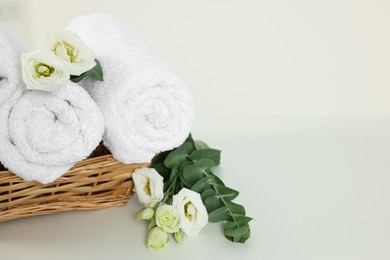 Photo of Soft folded towels and flowers on white table, space for text