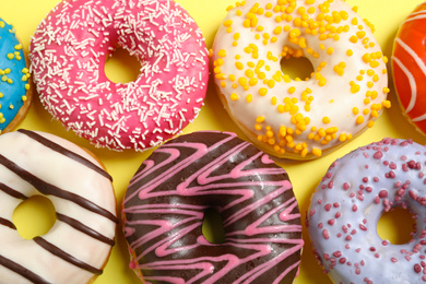 Photo of Delicious glazed donuts on yellow background, flat lay