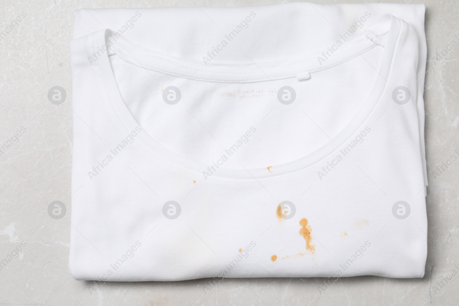 Photo of Dirty t-shirt with stains of sauce on light grey marble table, top view