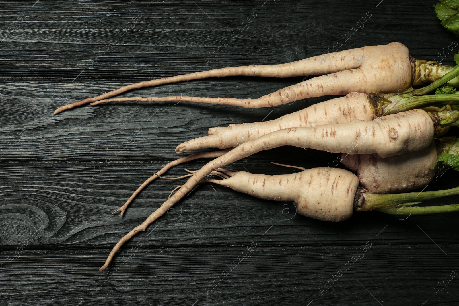 Photo of Tasty fresh ripe parsnips on black wooden table, flat lay