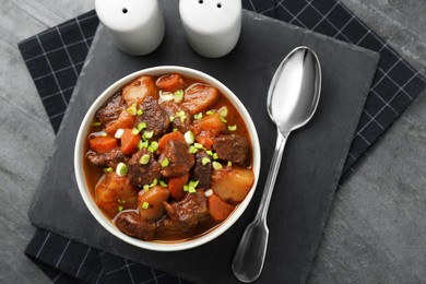 Photo of Delicious beef stew with carrots, green onions and potatoes served on grey table, flat lay