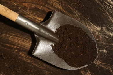 Photo of Metal shovel with fertile soil on dirty wooden surface, top view
