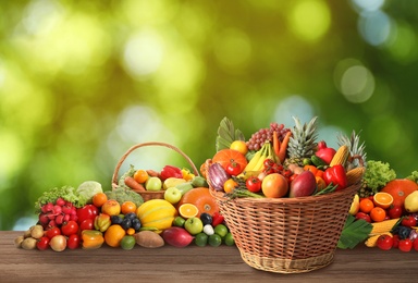 Image of Wicker baskets with different fresh organic vegetables and fruits on wooden table against blurred green background
