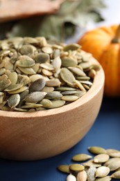 Wooden bowl with pumpkin seeds on blue table, closeup