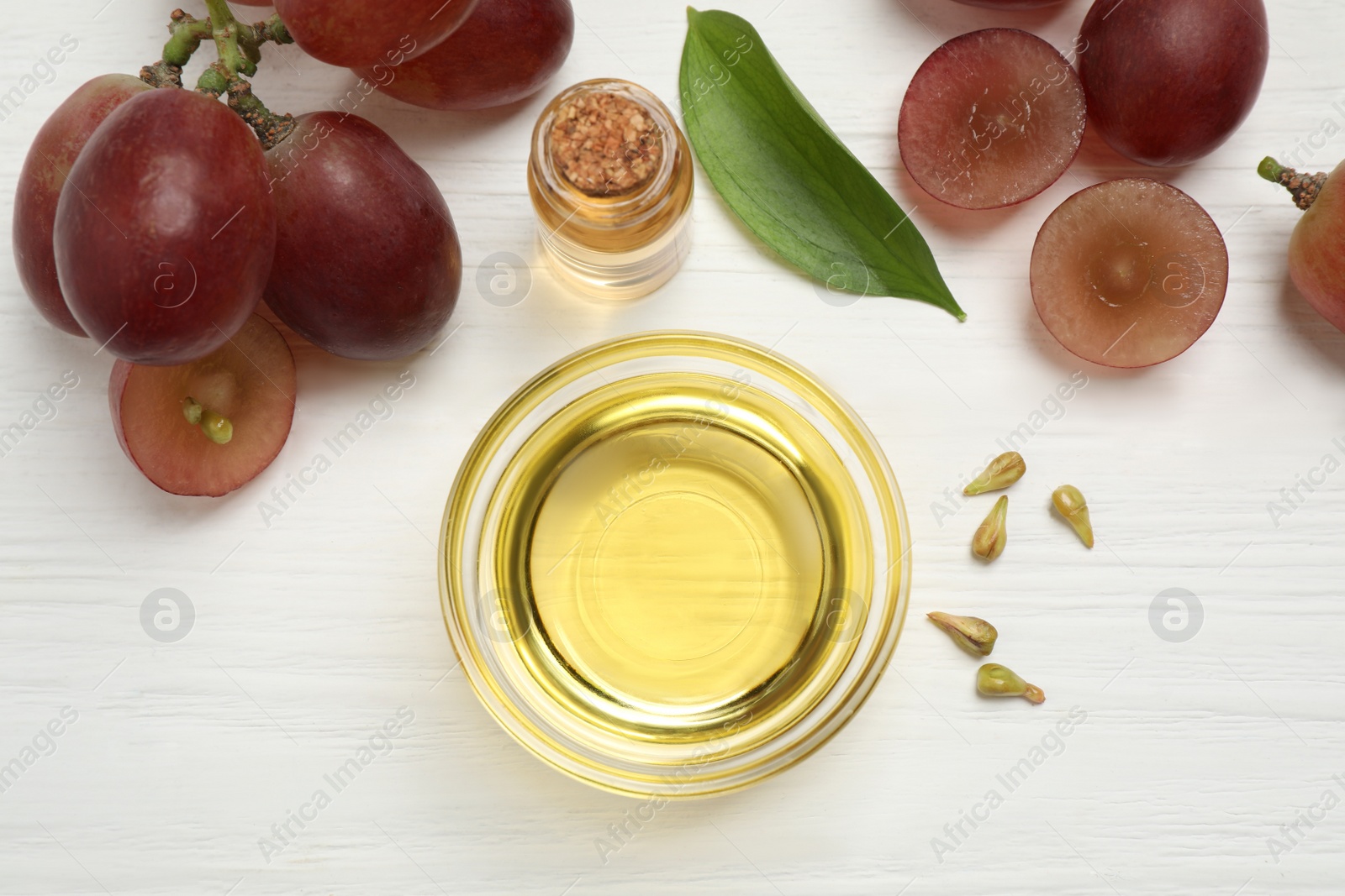 Photo of Flat lay composition with natural grape seed oil on white wooden table. Organic cosmetic