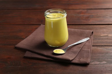 Photo of Glass jar and spoon with tasty mustard sauce on wooden table