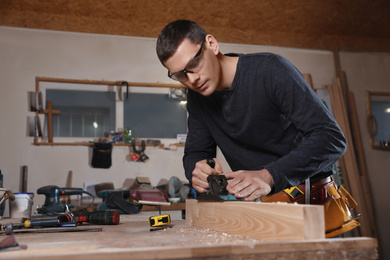 Professional carpenter grinding wooden plank with jack plane in workshop