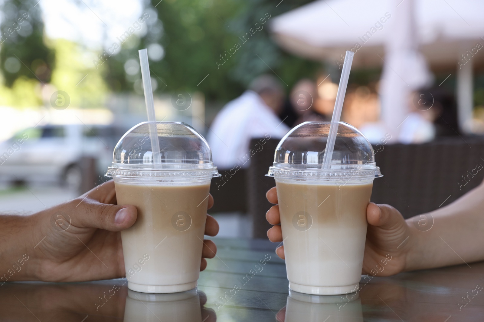 Photo of Man and woman with plastic takeaway cups of delicious iced coffee at table in outdoor cafe, closeup