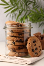 Glass jar with delicious chocolate chip cookies on white marble table