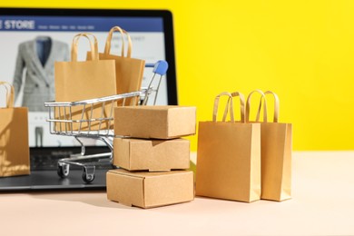 Photo of Online store. Purchases, mini shopping cart and laptop on beige table