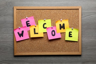 Photo of Corkboard with word Welcome on wooden table, top view