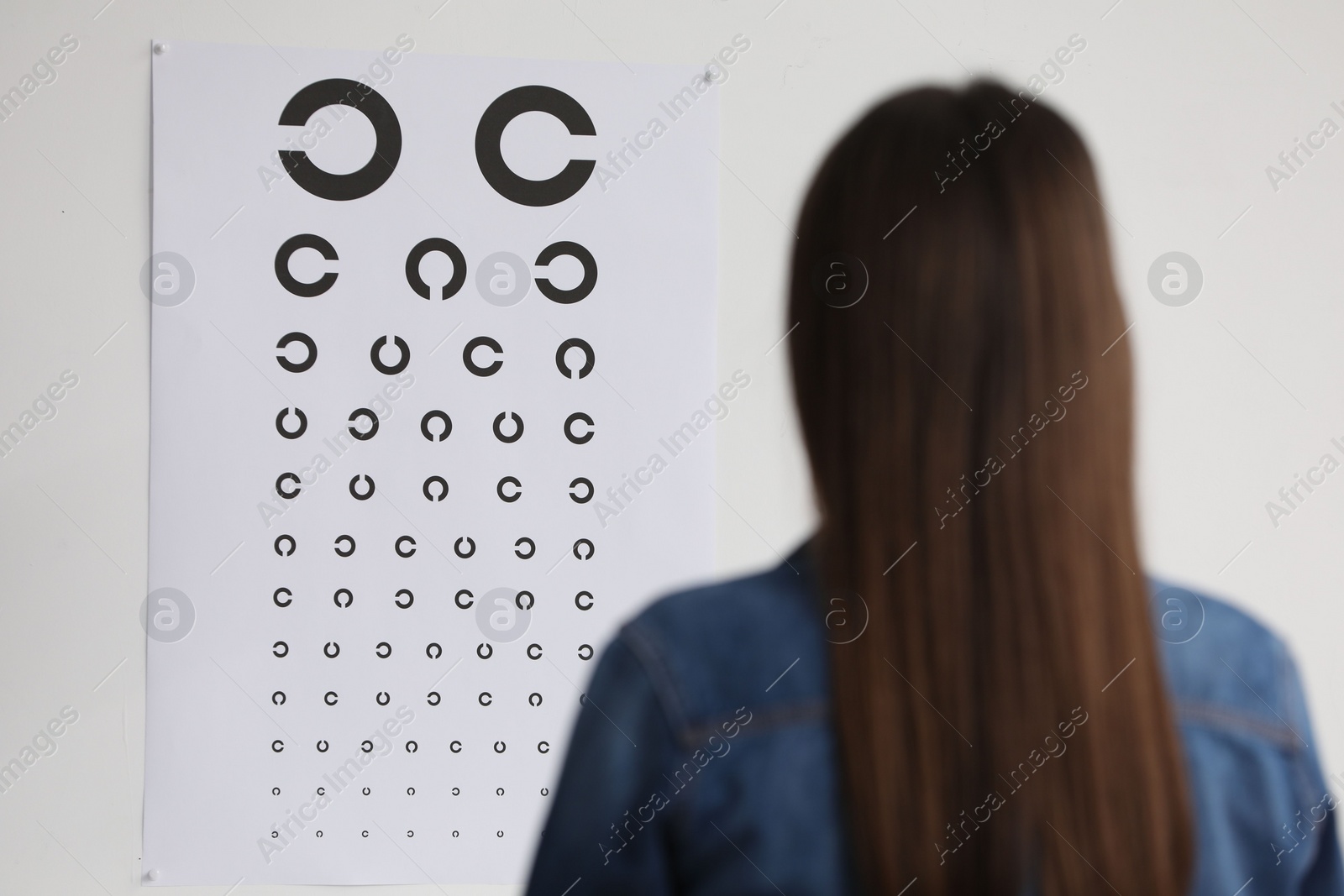 Photo of Eyesight examination. Young woman looking at vision test chart indoors, back view