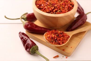 Chili pepper flakes and pods on white wooden table, closeup