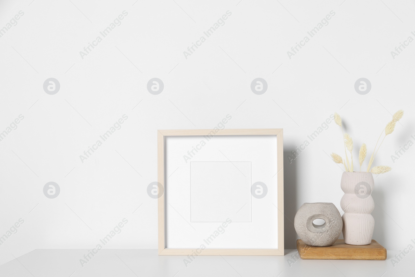 Photo of Empty photo frame and vase with dry decorative spikes on white table. Mockup for design