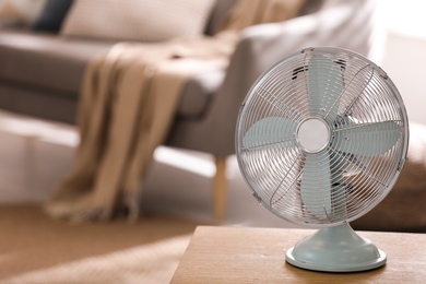 Photo of Modern electric fan on wooden table in living room. Space for text