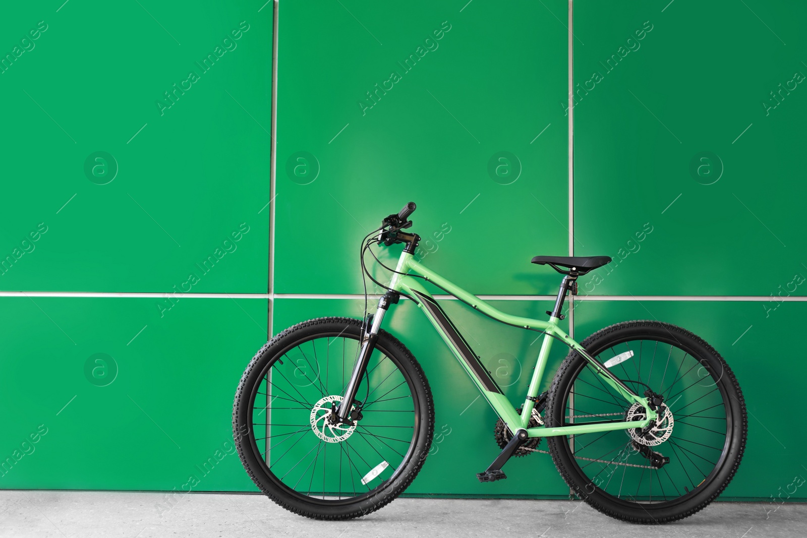 Photo of New modern color bicycle near green wall outdoors