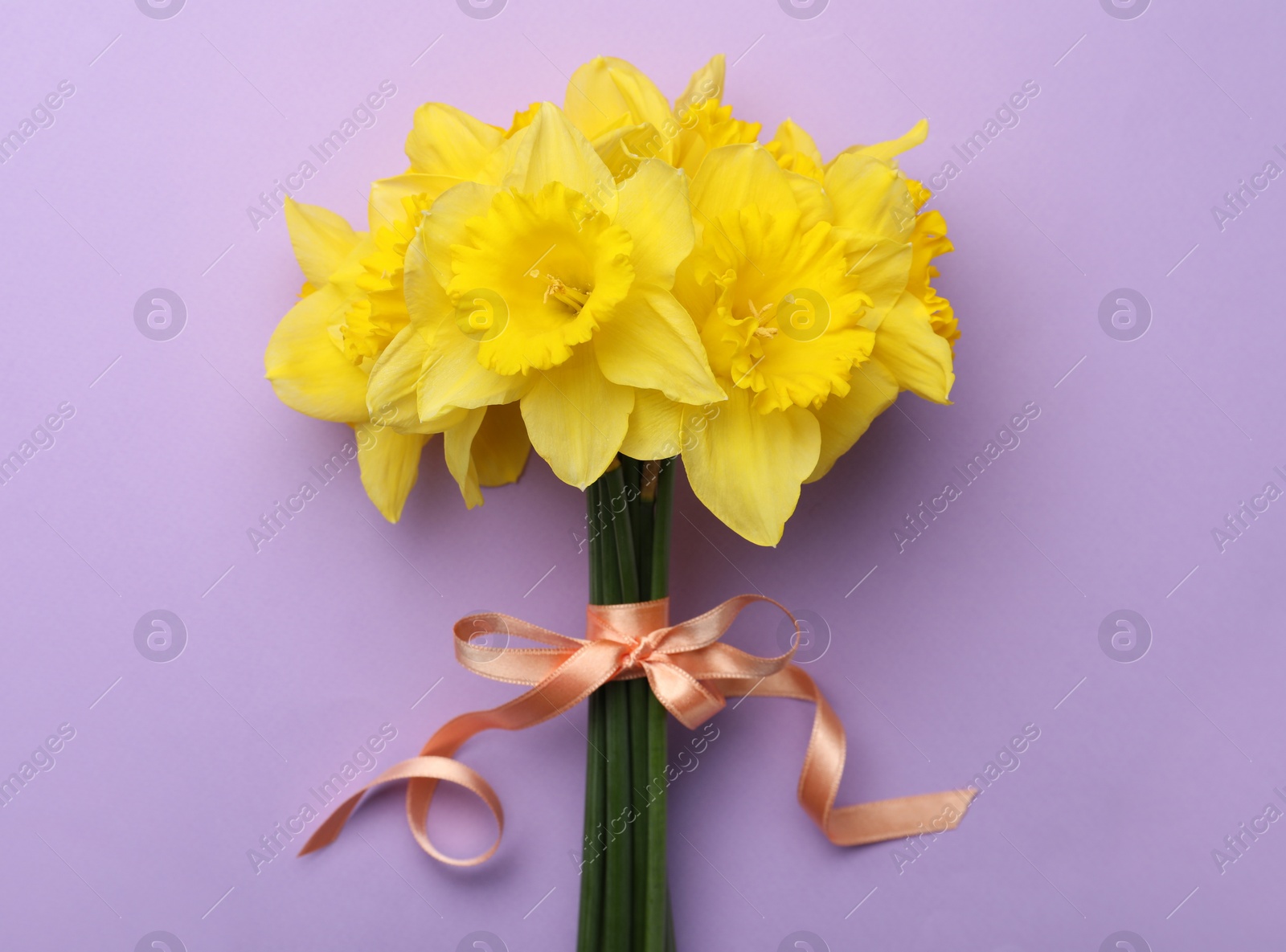 Photo of Beautiful daffodil bouquet on violet background, top view