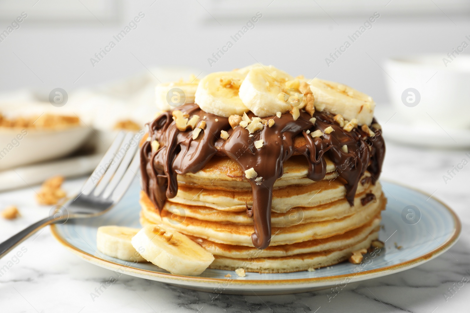 Photo of Tasty pancakes with chocolate spread, sliced banana and nuts served on table, closeup