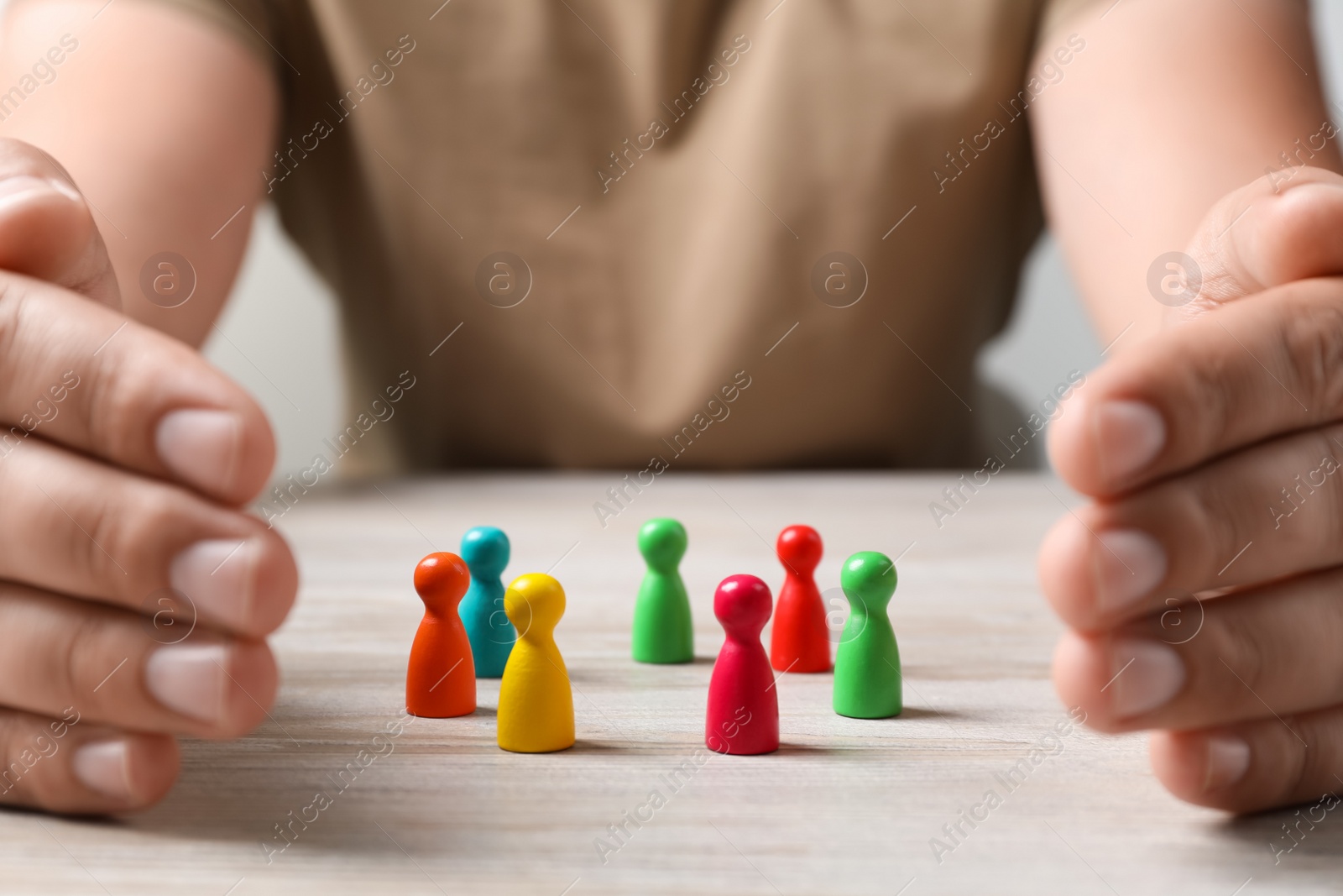 Photo of Woman protecting colorful pawns at white wooden table, closeup. Social inclusion concept