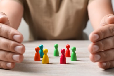 Woman protecting colorful pawns at white wooden table, closeup. Social inclusion concept