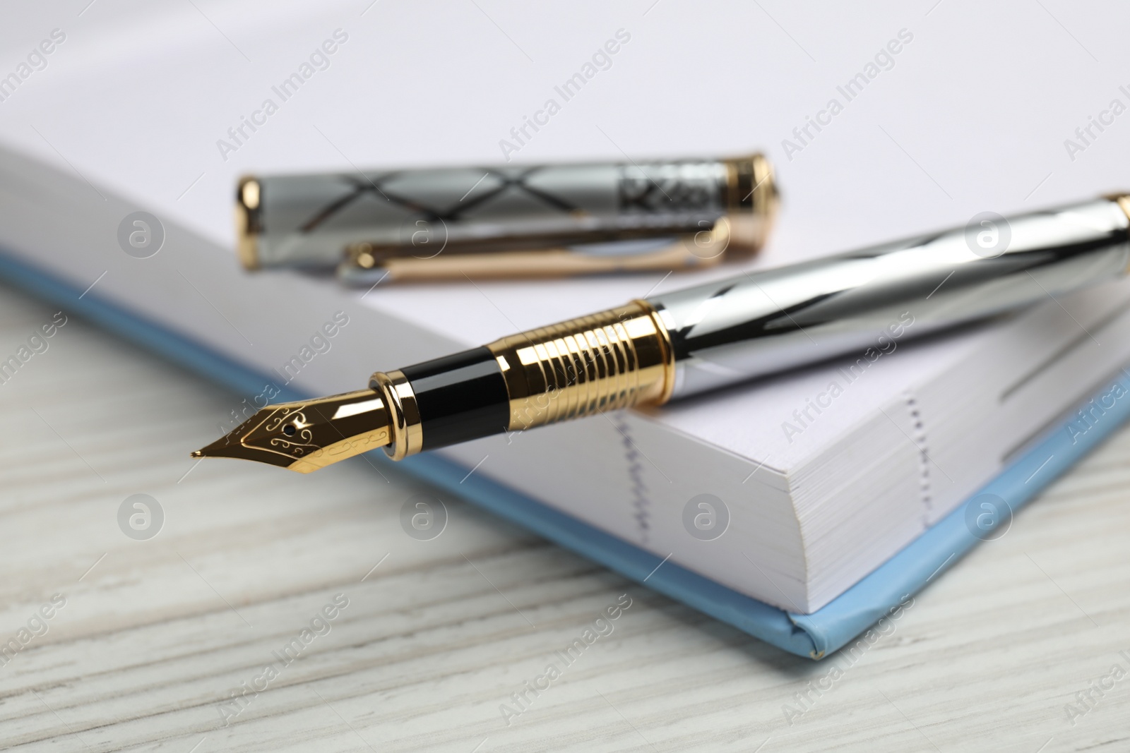 Photo of Beautiful fountain pen with ornate nib and notebook on white wooden table, closeup