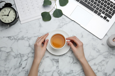 Woman with cup of tea at white marble table, top view