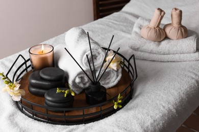 Photo of Aromatic reed air freshener, rolled towels, spa stones and candle on bed indoors