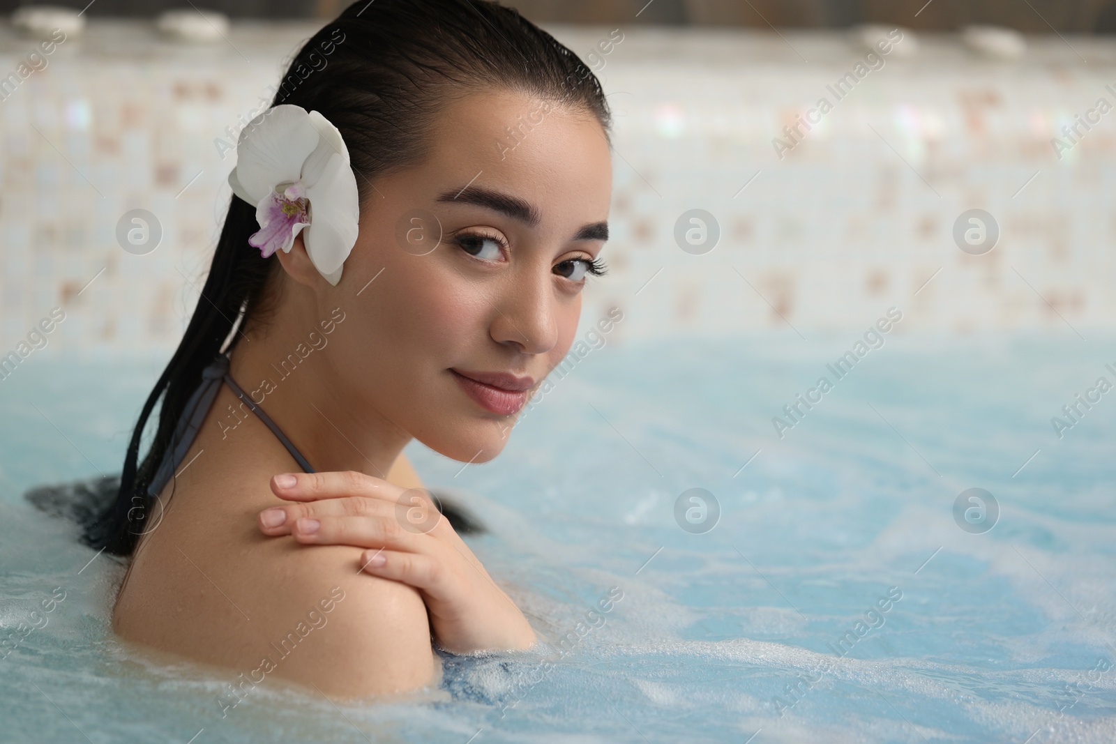 Photo of Beautiful woman with orchid flower in spa swimming pool, space for text