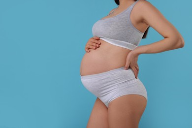 Photo of Pregnant woman in comfortable maternity underwear on light blue background, closeup. Space for text