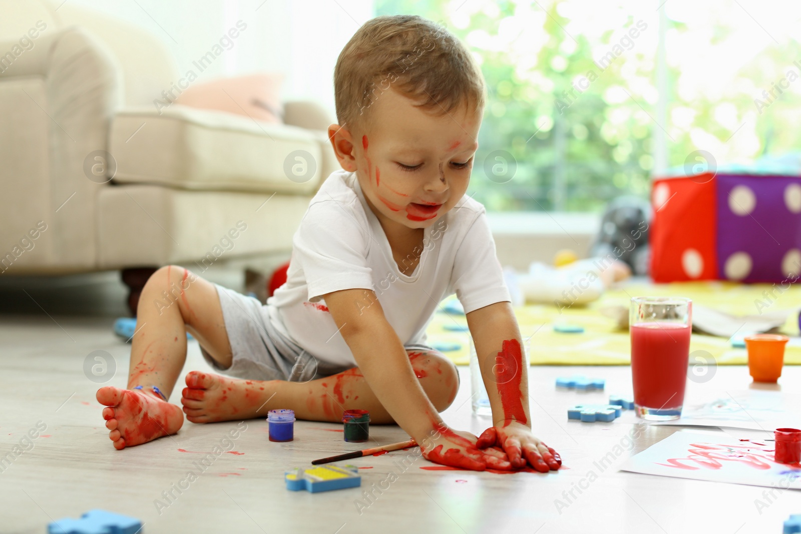 Photo of Cute little boy playing with paints on floor in living room