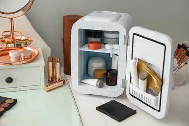 Photo of Cosmetics refrigerator and skin care products on white vanity table indoors