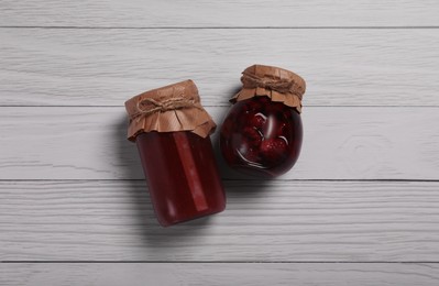 Photo of Jars with preserved fruit jams on white wooden table, flat lay