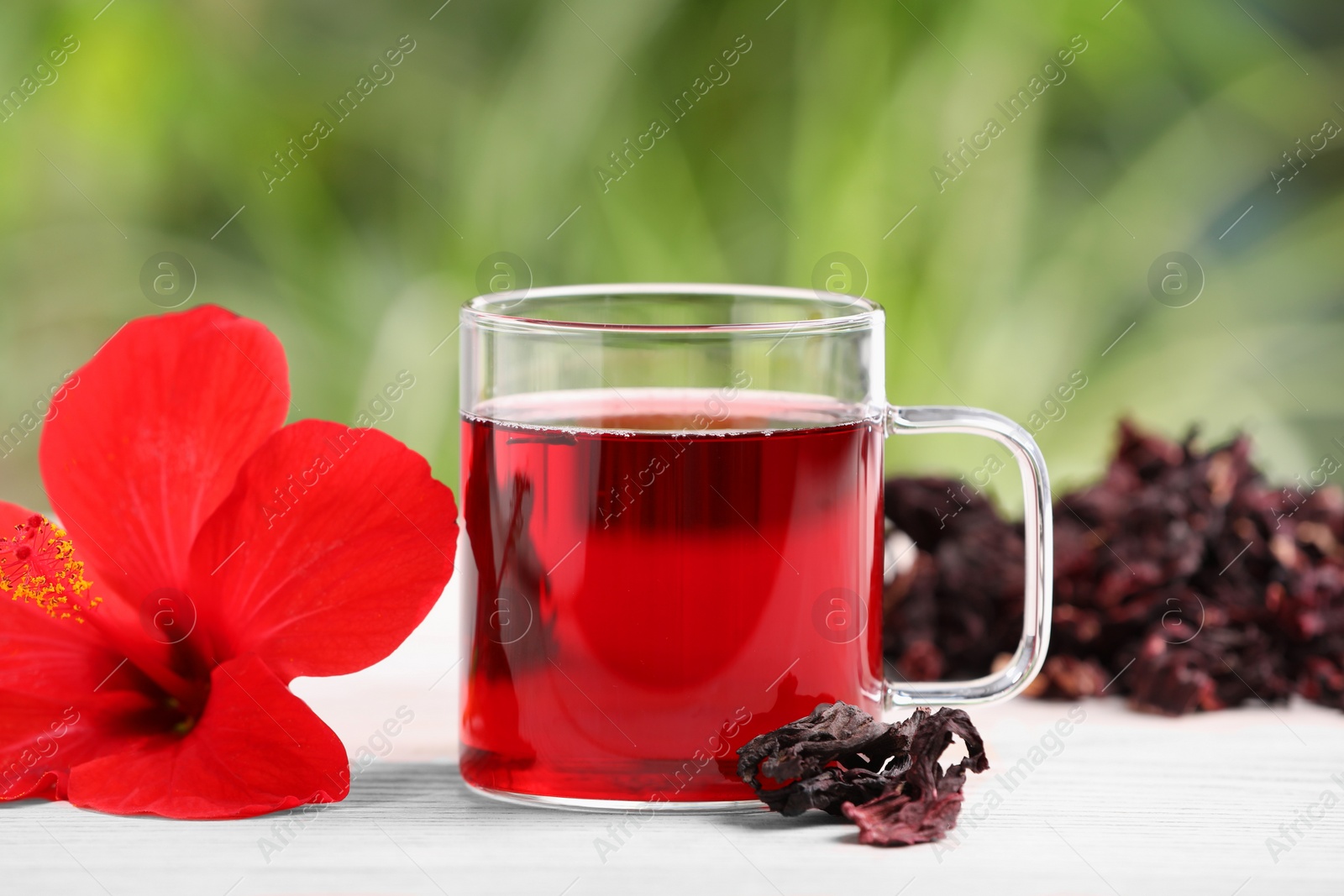 Photo of Delicious hibiscus tea and flowers on white wooden table outdoors, closeup