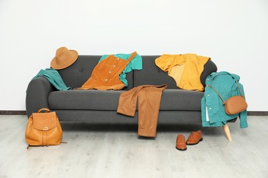 Photo of Messy pile of clothes on sofa and shoes in living room