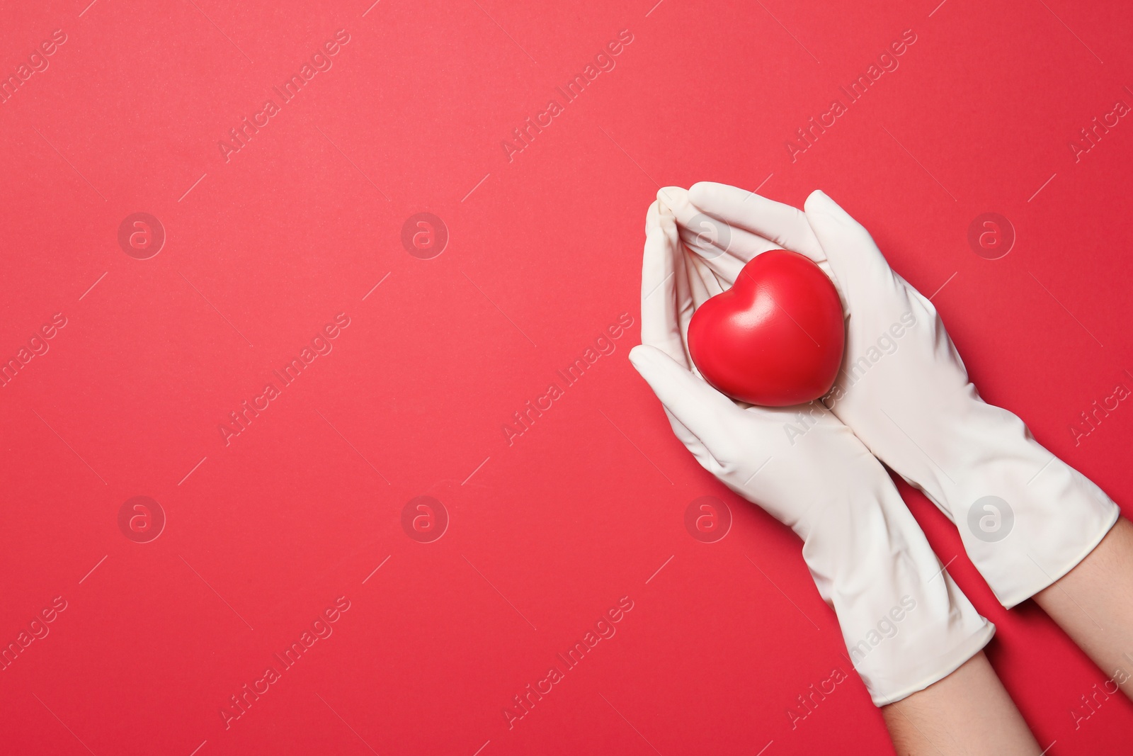 Photo of Doctor in medical gloves holding heart on color background, top view. Space for text