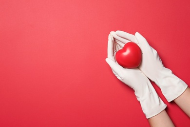 Doctor in medical gloves holding heart on color background, top view. Space for text