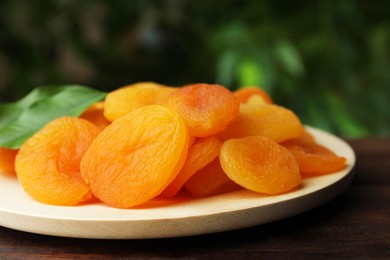 Photo of Plate of tasty apricots on wooden table against blurred green background. Dried fruits
