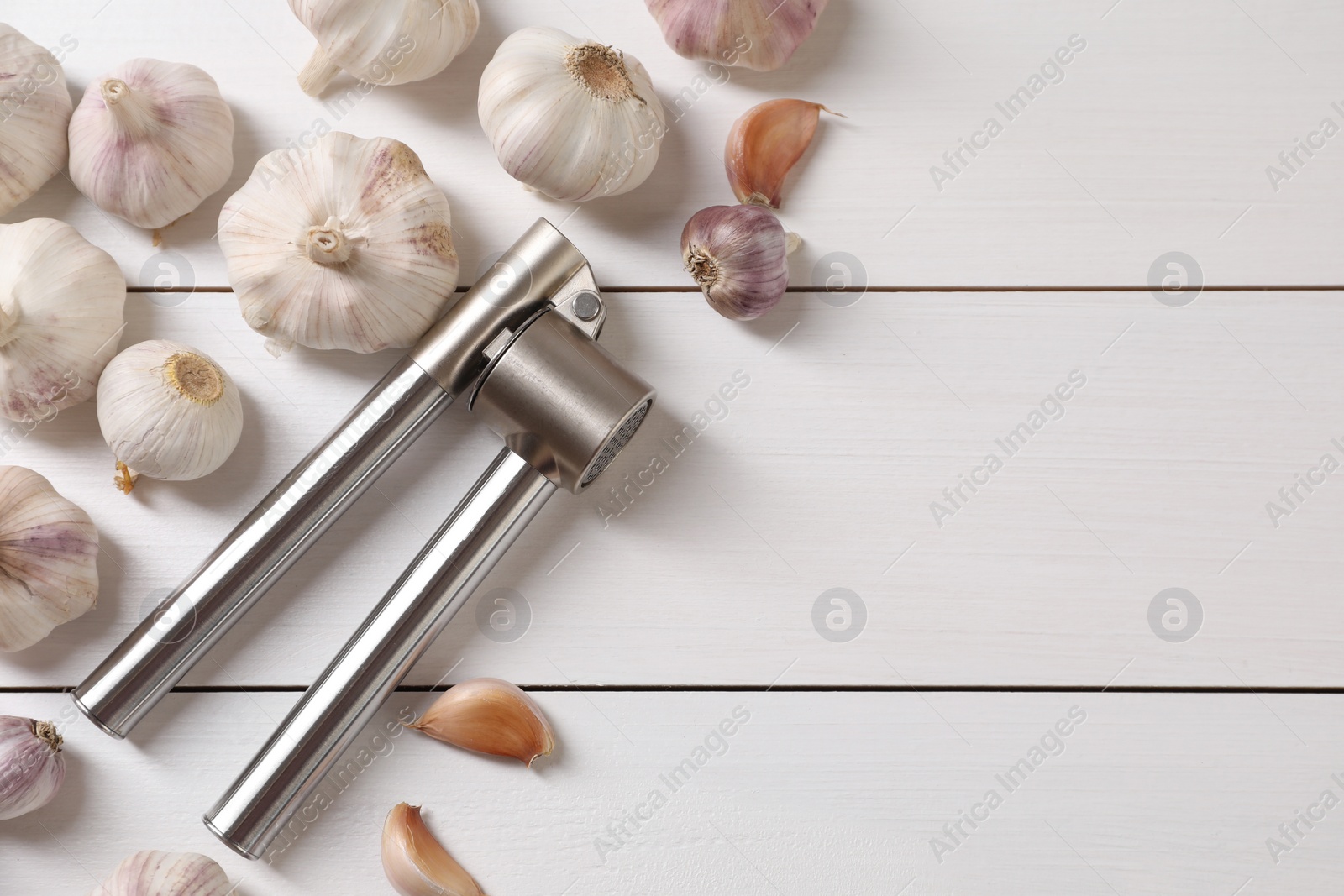 Photo of Metal press and garlic on white wooden table, flat lay. Space for text