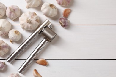 Metal press and garlic on white wooden table, flat lay. Space for text