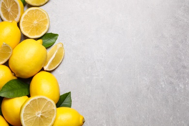 Photo of Many fresh ripe lemons with green leaves on light grey table, flat lay. Space for text