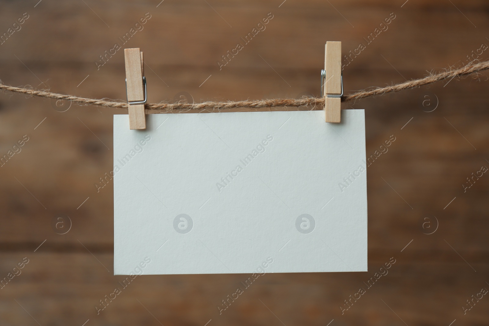 Photo of Clothespins with blank notepaper on twine against wooden background. Space for text