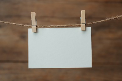 Photo of Clothespins with blank notepaper on twine against wooden background. Space for text