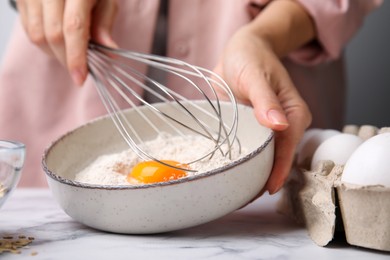 Photo of Woman mixing egg with flour at white marble table in kitchen, closeup. Cooking oatmeal dough