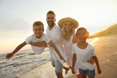 Photo of Happy family having fun on sandy beach near sea at sunset