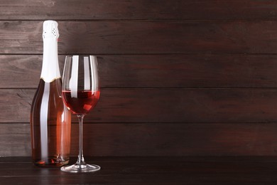Bottle and glass of delicious rose wine on table against wooden background. Space for text