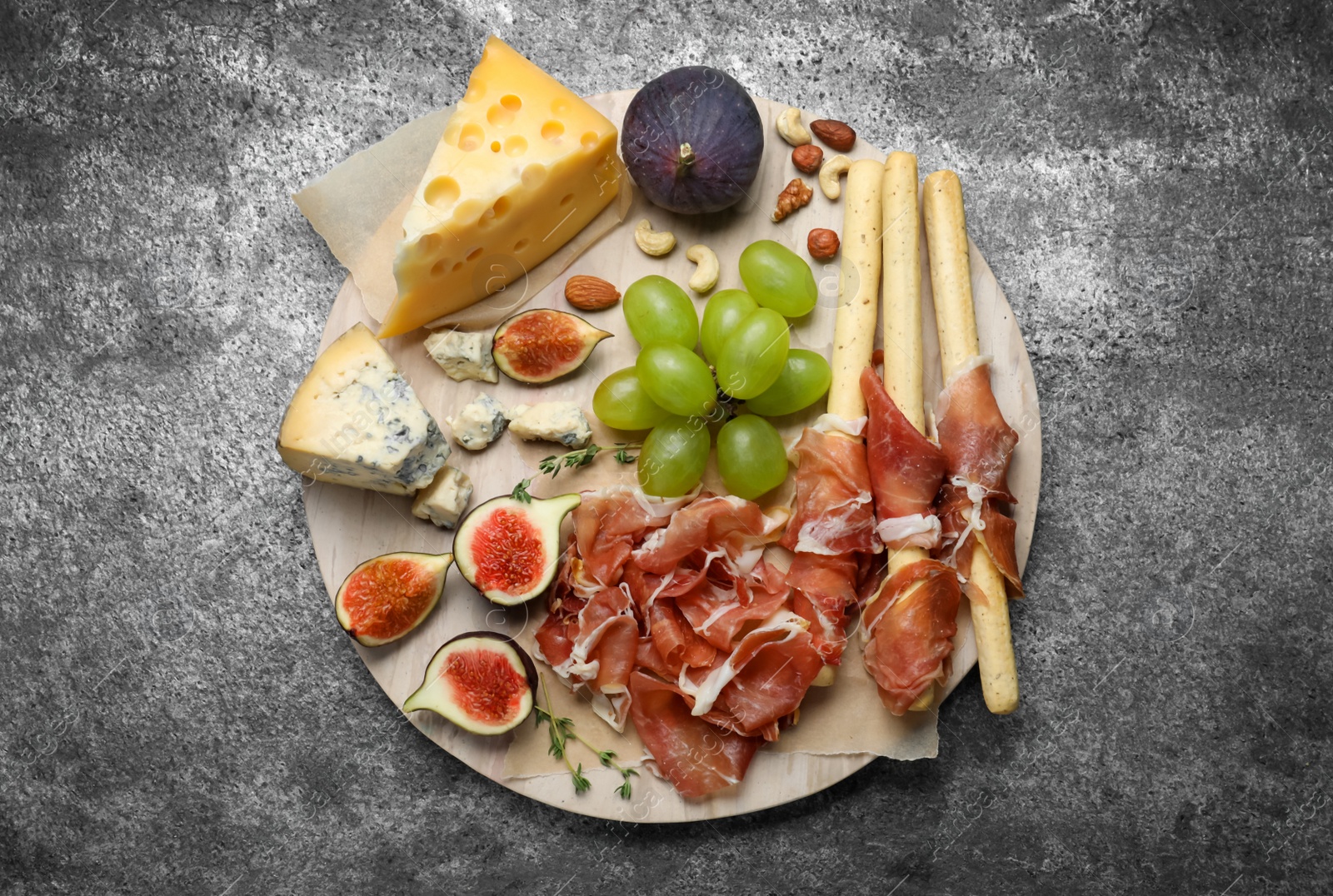 Photo of Board with delicious figs, cheese, grapes and bread with proscuitto on grey table, top view