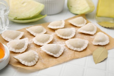 Photo of Raw dumplings (varenyky) with tasty filling and flour on white tiled table, closeup