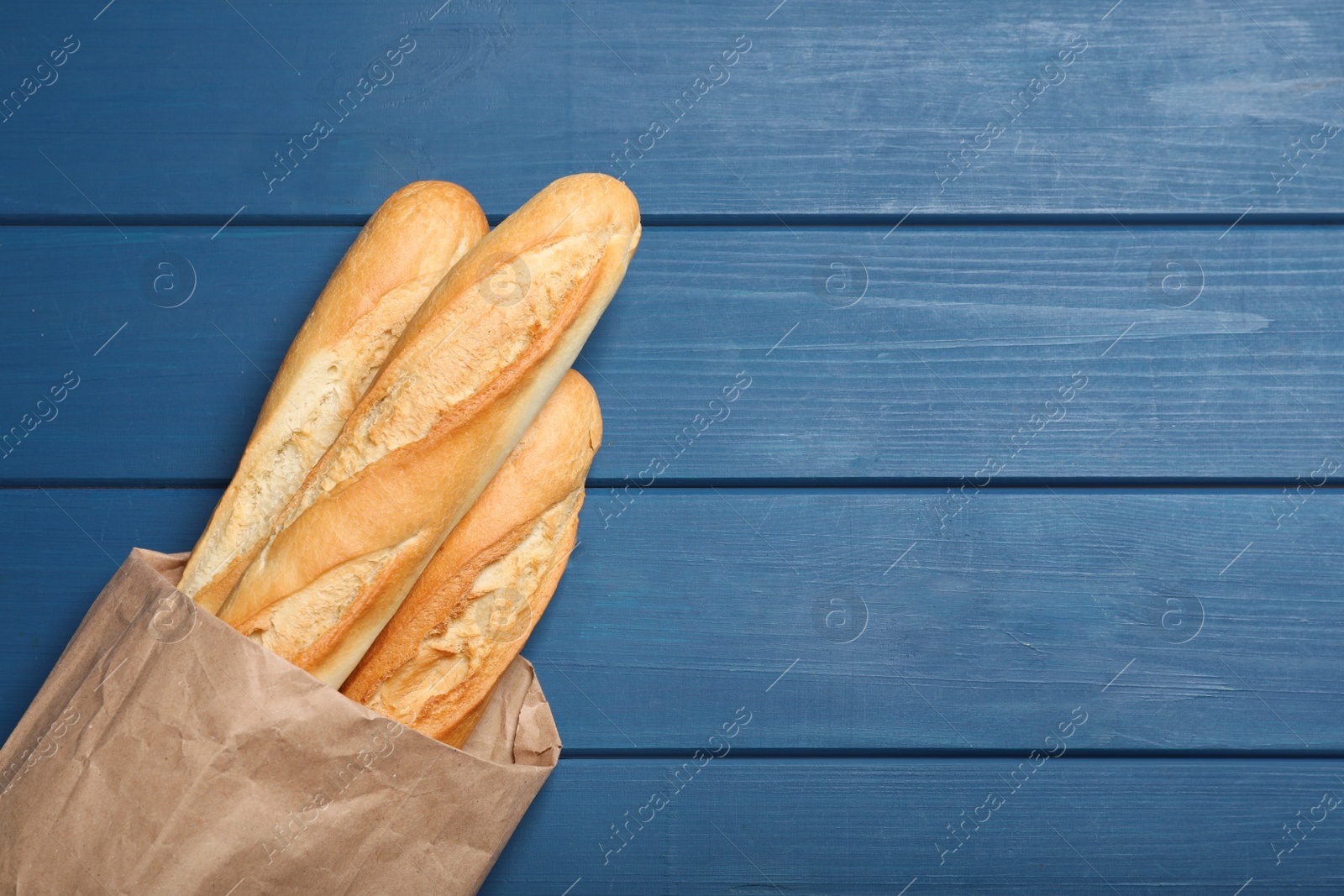 Photo of Tasty baguettes in package on blue wooden table, top view. Space for text