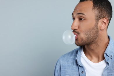 Young man blowing bubble gum on light grey background. Space for text