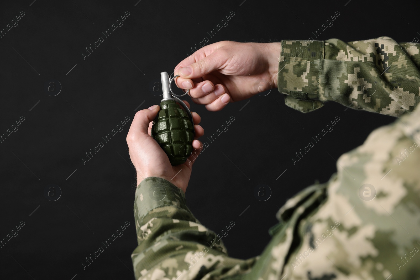 Photo of Soldier pulling safety pin out of hand grenade on black background, closeup. Military service